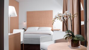 Habitación de hotel moderna con cama, sofá, escritorio y una mesa redonda con una orquídea en maceta.