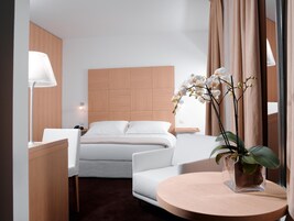 Habitación de hotel moderna con cama, sofá, escritorio y una mesa redonda con una orquídea en maceta.