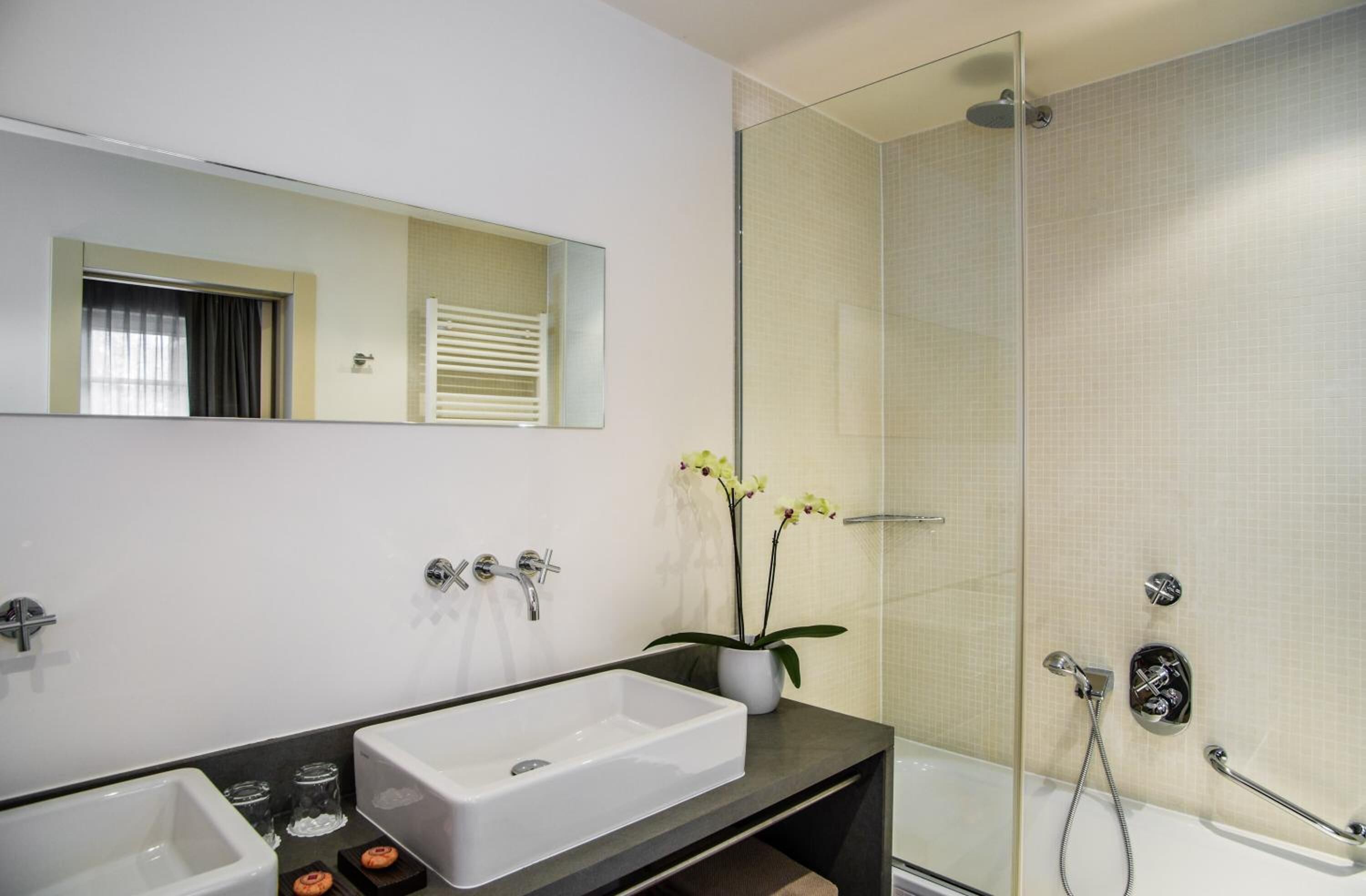 Ein modernes Badezimmer mit einem großen, weißen Waschbecken, einer Duschkabine aus Glas und einer Topforchidee.