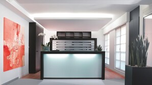 Un mostrador de recepción moderno con un panel iluminado, un cuadro abstracto de gran tamaño y plantas en macetas.