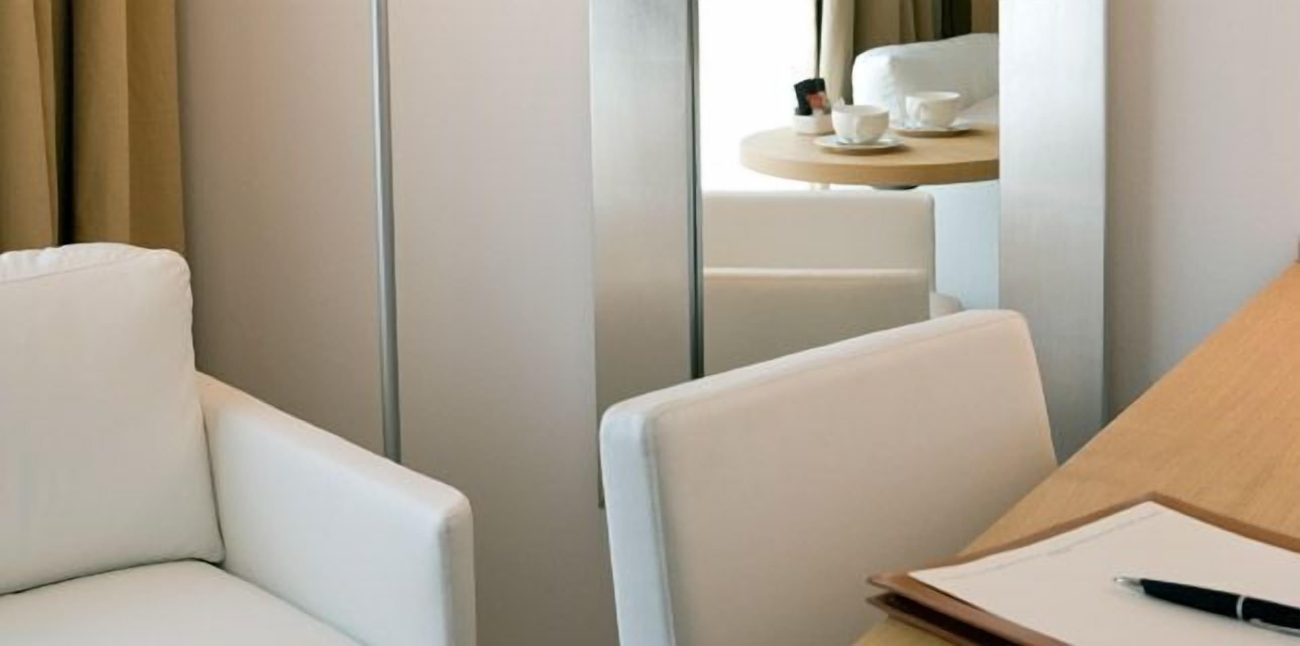 Een hotelkamer met een bed, een nachtkastje met kop en schotel, en een stoel.