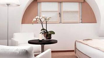 A modern bedroom with a curved ceiling, a round table with a plant, a white sofa, and a bed with a beige headboard.