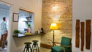 A kitchen with a brick wall, a green chair, and a bar area with stools. - Friends Hostel and Apartments Budapest (Budapest)