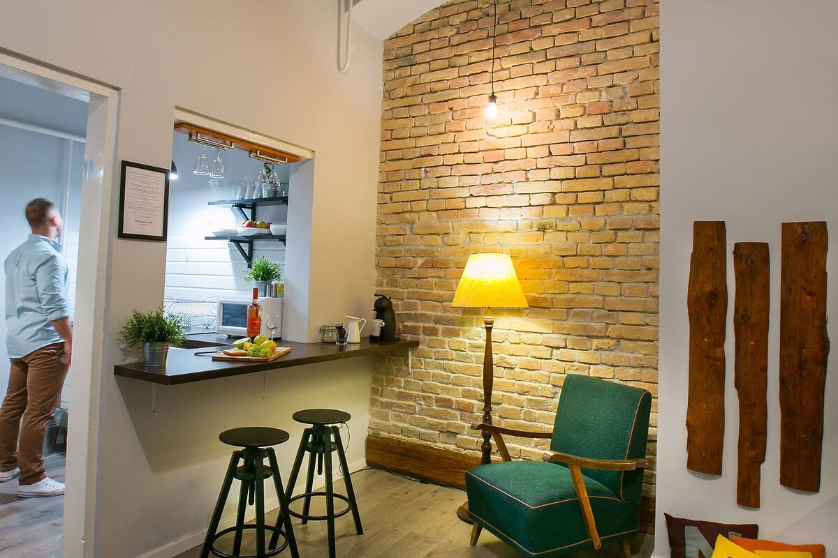 A kitchen with a brick wall, a green chair, and a bar area with stools.