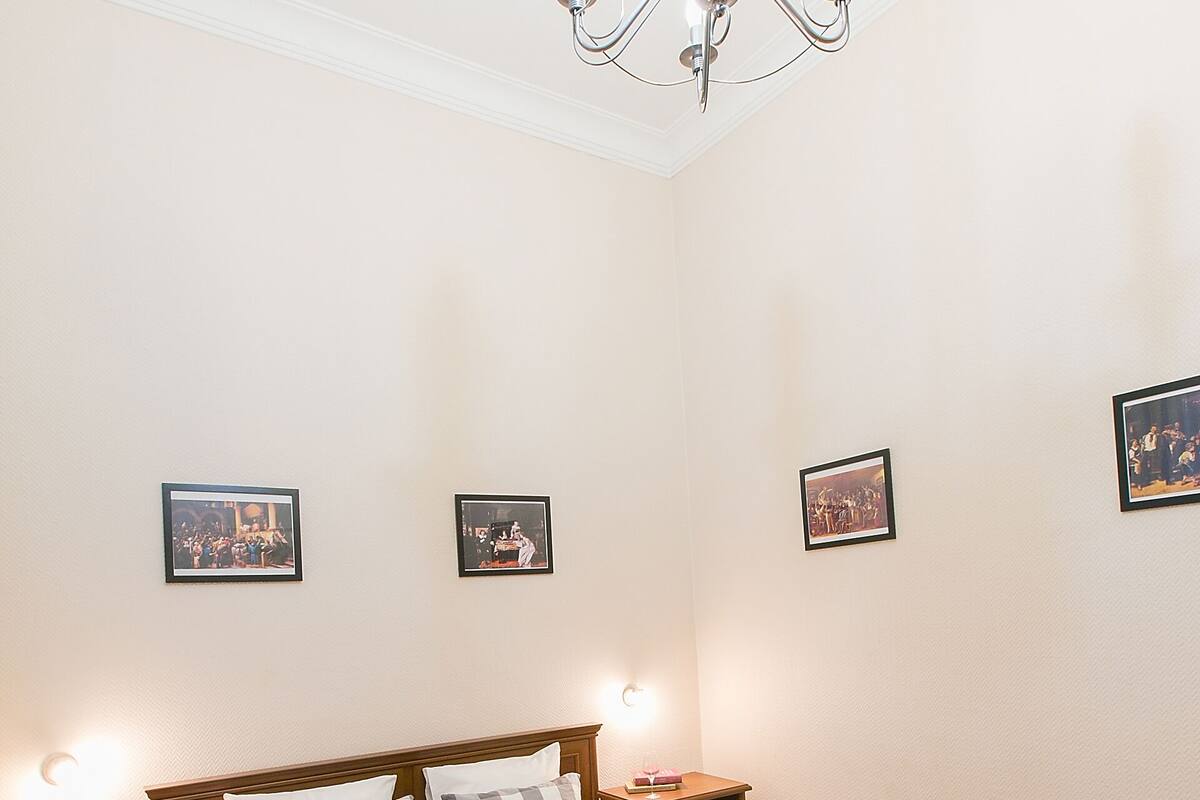A bedroom with a wooden bed, two bedside tables, a chandelier, and framed pictures on the wall.