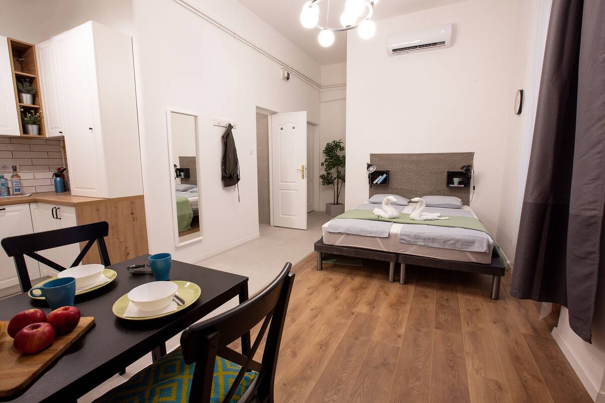A compact hotel room with a bed, bedside table, and a small kitchenette.