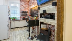 A modern kitchen with a brick wall, a large screen displaying a gaming interface, and a chalkboard menu. - Friends Hostel and Apartments Budapest (Budapest)