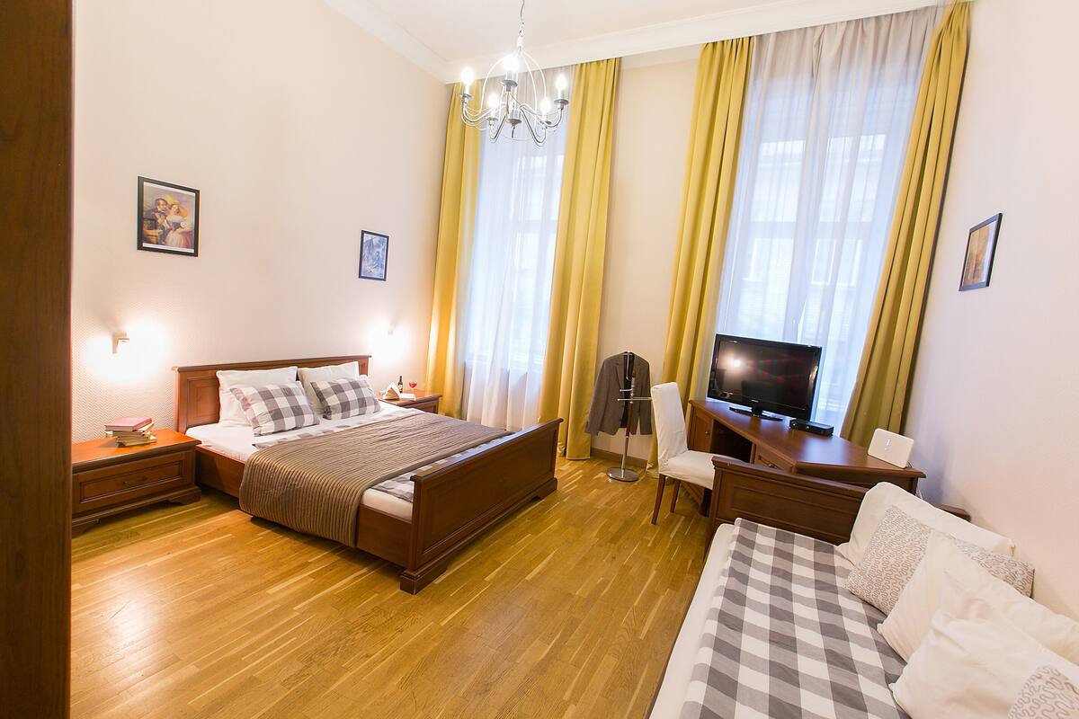 A hotel room with a wooden bed, a desk with a TV, a chair, and a desk lamp.