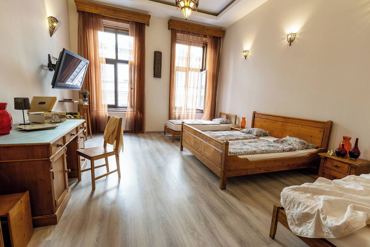 A bedroom with a wooden bed, a desk with a computer, and a TV mounted on the wall.