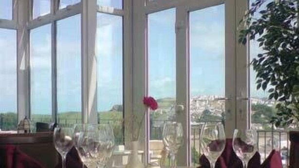 A dining area with a table set for two, large windows, and a view of the countryside. - Pendeen Hotel (Newquay)