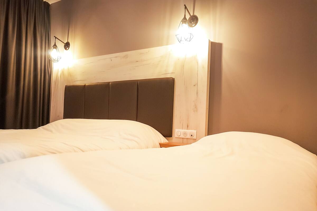 A hotel room with two beds, a wooden headboard, and two wall-mounted lights.