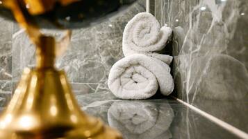 Une salle de bain aux murs de marbre, avec un robinet doré et des serviettes blanches pliées.