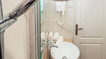 Un baño con cabina de ducha de vidrio, un lavamanos blanco y un perchero con toallas dobladas ordenadamente.