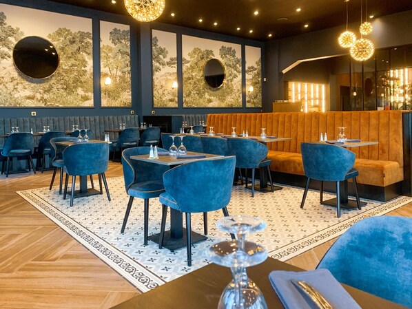 Un restaurante con sillas de terciopelo azul, mesas redondas y un suelo estampado.