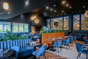 Un restaurante moderno con asientos azul y naranja, ventanas amplias y un techo decorativo.
