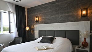 Et moderne hotelværelse med en stor seng, et natbord med en vase og udsigt til det fri.