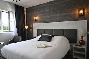 Habitación de hotel moderna con una cama grande, una mesita de noche con un florero y vistas al exterior.