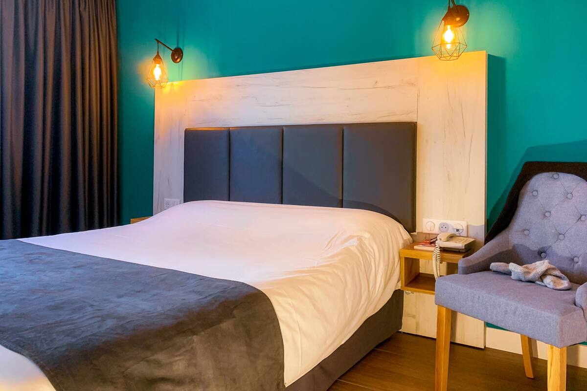 A hotel room with a large bed, a wooden nightstand, a chair, and two wall-mounted lamps.