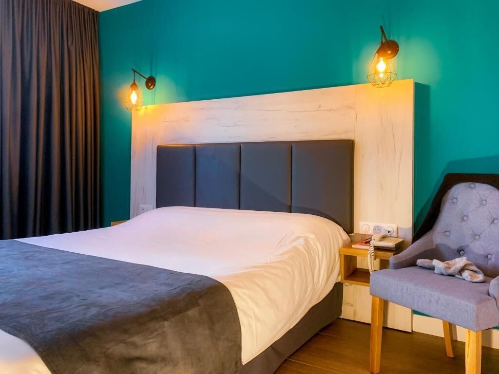 Ein Hotelzimmer mit einem Bett, einem Sessel, einem Nachttisch und einer Wandlampe.