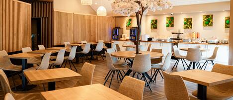 Un restaurante moderno con mesas y sillas de madera, un árbol decorativo y obras de arte en las paredes.