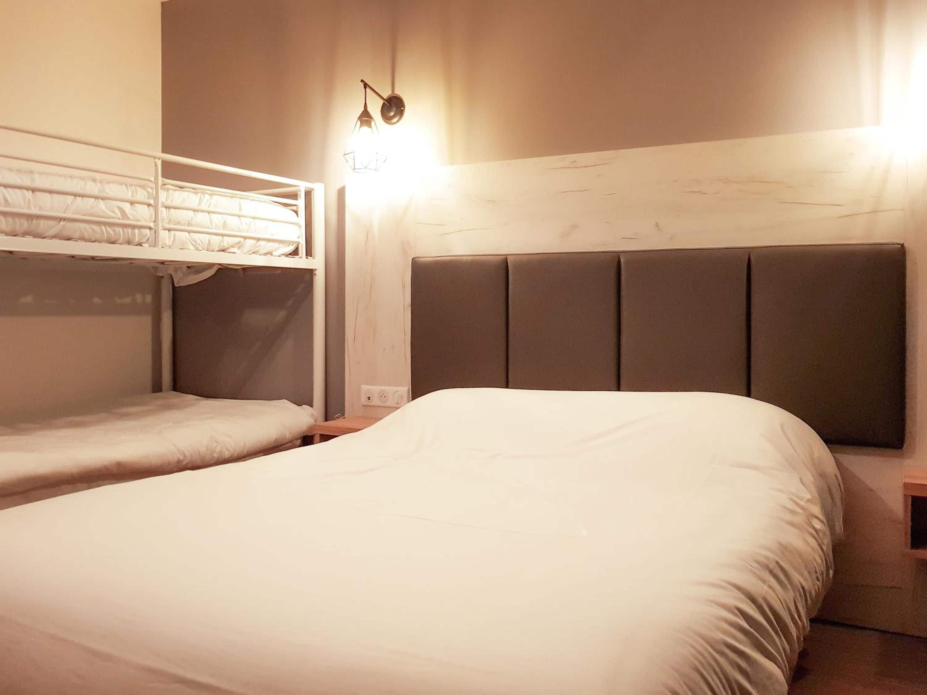 A hotel room with a bunk bed, a single bed, and a bedside table.