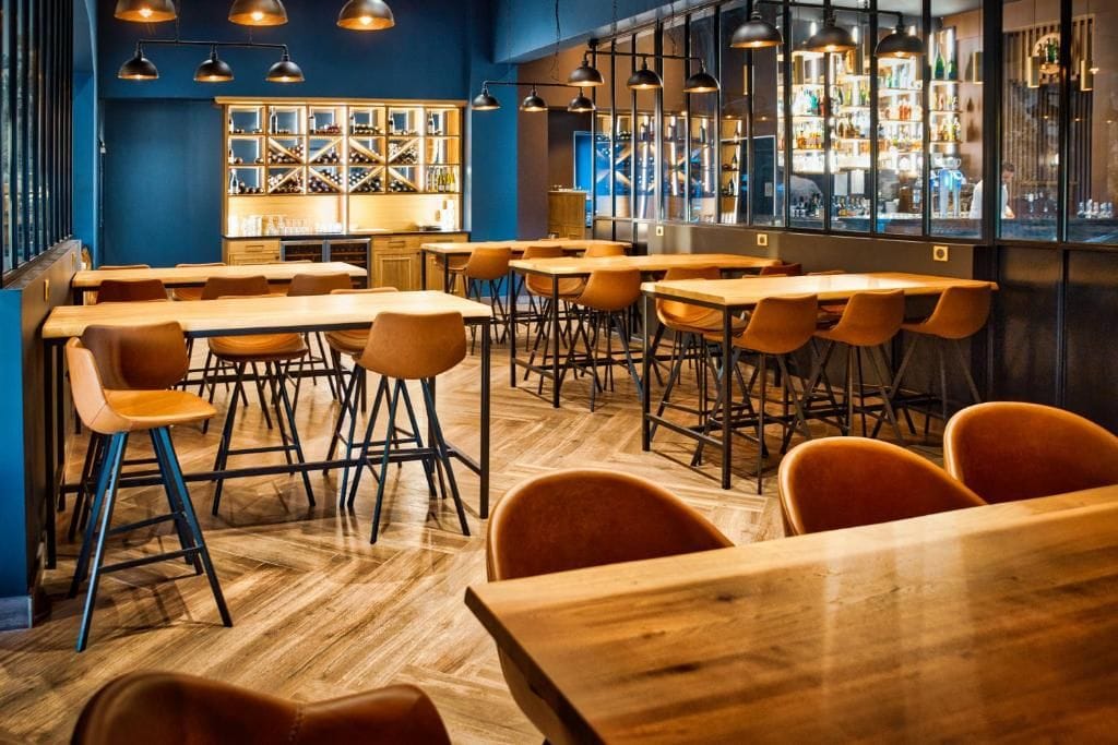 A bar area with wooden tables and chairs, a wine display, and pendant lighting.