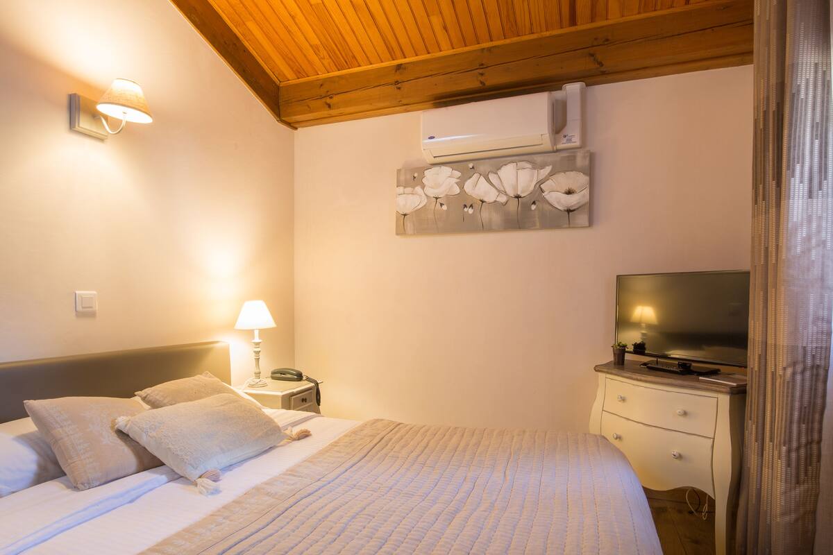 Un dormitorio con cama, lámpara de noche, televisor y aire acondicionado instalado en la pared.