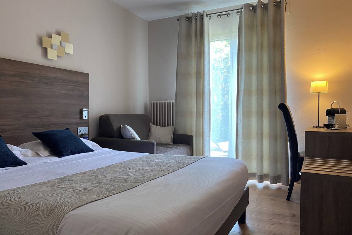 Habitación de hotel con una cama grande, un sofá, un escritorio con lámpara y vistas al exterior.