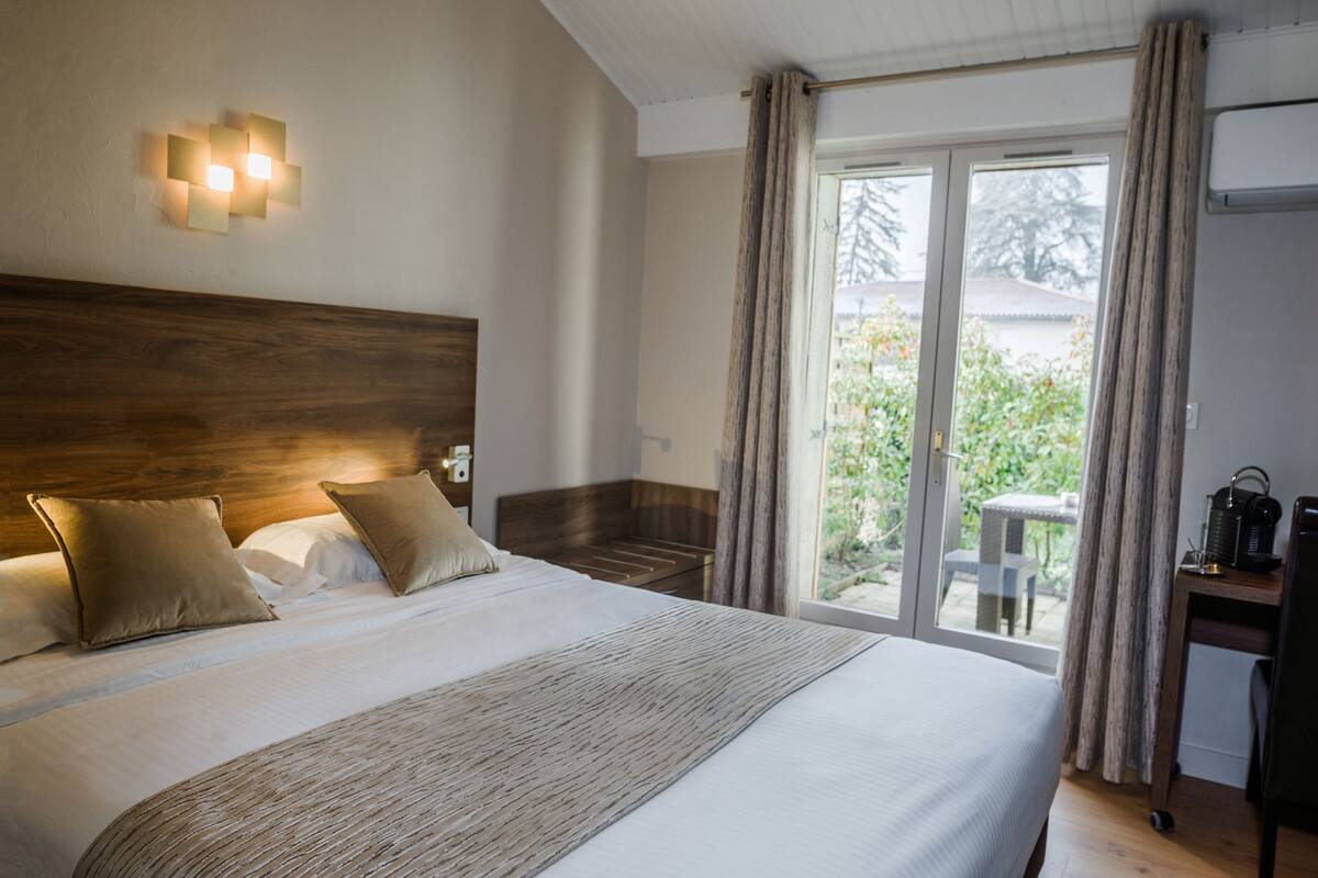 Habitación de hotel con una cama grande, cabecera de madera, mesita de noche, escritorio con lámpara y puerta corrediza de vidrio que da a un espacio exterior.