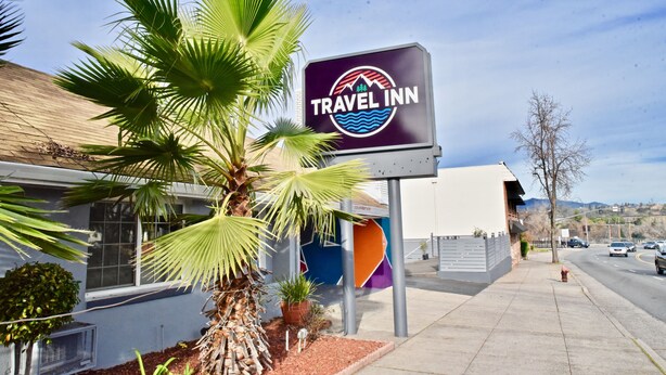 A Travel Inn sign with a mountain and waves logo, palm trees, and a clear sky. - Travel Inn (Redding)