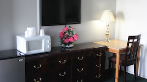A hotel room with a flat-screen TV mounted on the wall, a microwave on a wooden dresser, a table with a lamp, and a chair. - Travel Inn (Redding)