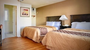 A hotel room with two beds, a nightstand, a lamp, and a framed picture on the wall. - Travel Inn (Redding)