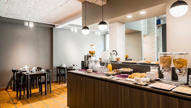 Ein Frühstücksbuffet mit verschiedenen Speisen und einer Kaffeemaschine. Im Hintergrund sind Tische und Stühle zu sehen.