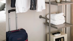 Ein Hotelzimmer mit Kleiderschrank, Koffer, Fernbedienung und ordentlich gefalteten Handtüchern.