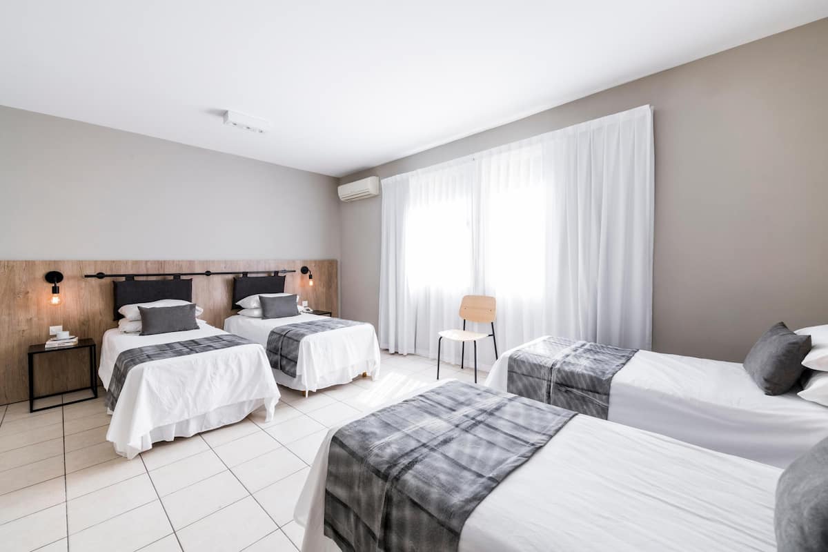 Ein Hotelzimmer mit zwei Betten, einem kleinen Tisch, einem Stuhl und einem Fenster mit Vorhängen.