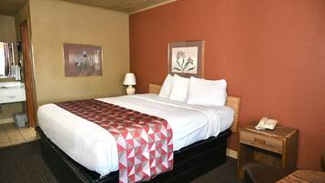 A hotel room with a bed, a nightstand with a phone, a lamp, and two framed pictures on the wall.