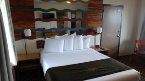 Habitación de hotel con cama, mesita de noche, lámpara, armario y espejo de diseño ondulado.