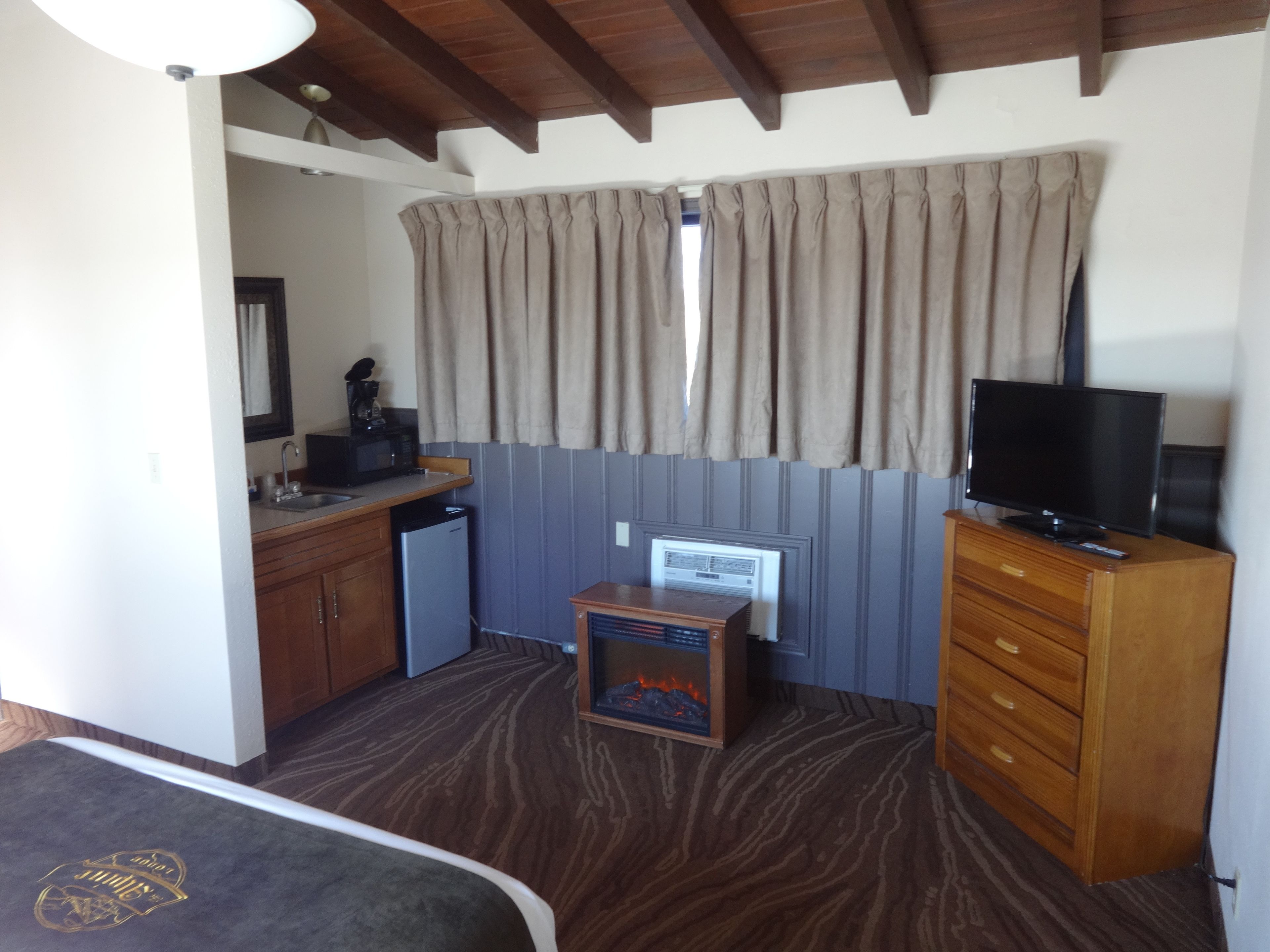 Quarto compacto com cozinha compacta, televisão, aquecedor pequeno e janela com cortinas.
