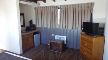 Quarto compacto com cozinha compacta, televisão, aquecedor pequeno e janela com cortinas.