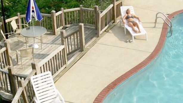 Un área de piscina con sillones de descanso y una mesita, rodeada por una terraza de madera y una cerca.