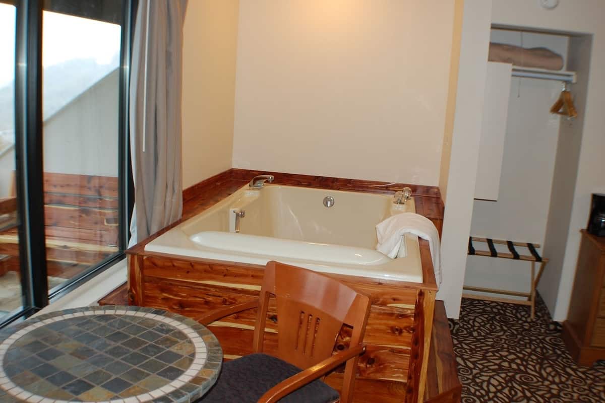 A bathroom with a wooden bathtub, a chair, and a small round table.