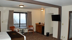 Habitación de hotel con una cama, dos sillas, una mesita, un lavamanos y una televisión.