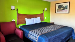 A hotel room with a bed, a red armchair, a wooden headboard, and a framed picture on the wall. - Royal Inn Linden (Linden)