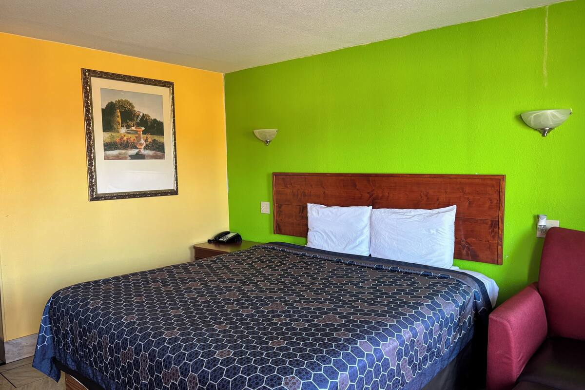 Una habitación con una cama, una mesita de noche, un cuadro enmarco y una pared verde.