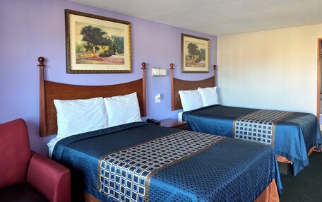 A hotel room with two beds, a red chair, and two framed landscape paintings on the wall.