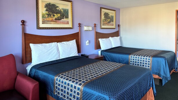 A hotel room with two beds, a red chair, and two framed landscape paintings on the wall. - Royal Inn Linden (Linden)