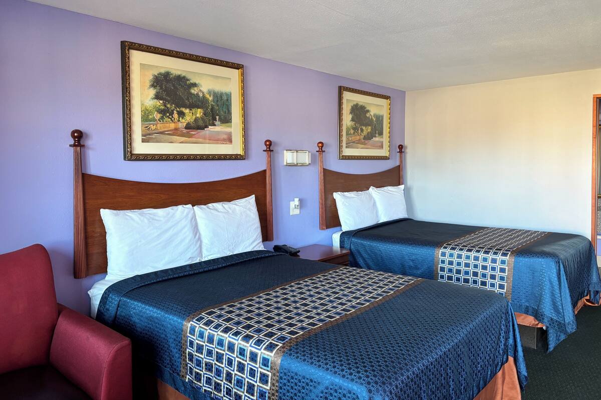 Habitación de hotel con dos camas, una silla roja y dos cuadros de paisajes en la pared.