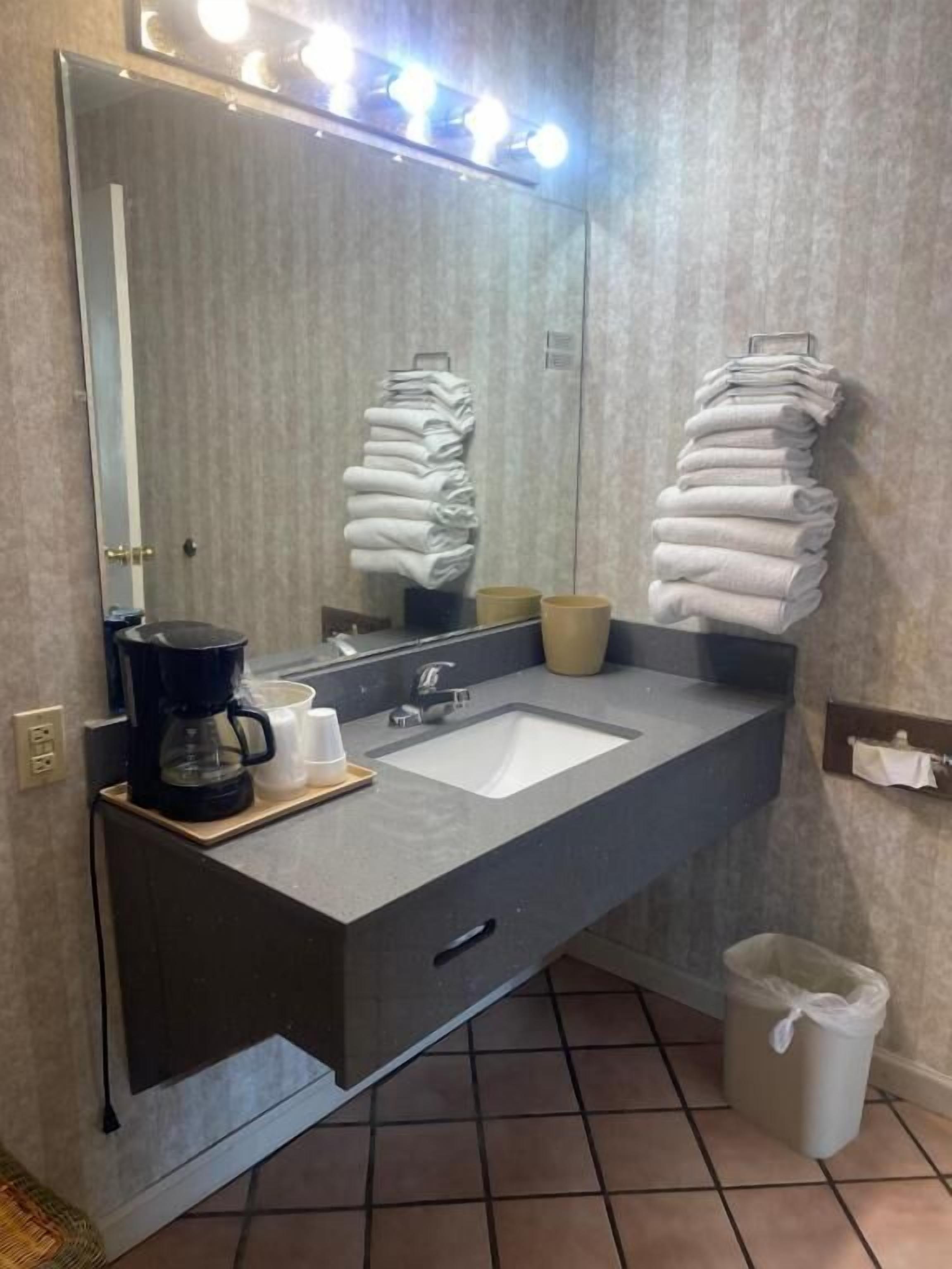 A bathroom with a large mirror, a sink, a coffee maker, and towels.