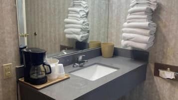 A bathroom with a large mirror, a sink, a coffee maker, and towels.
