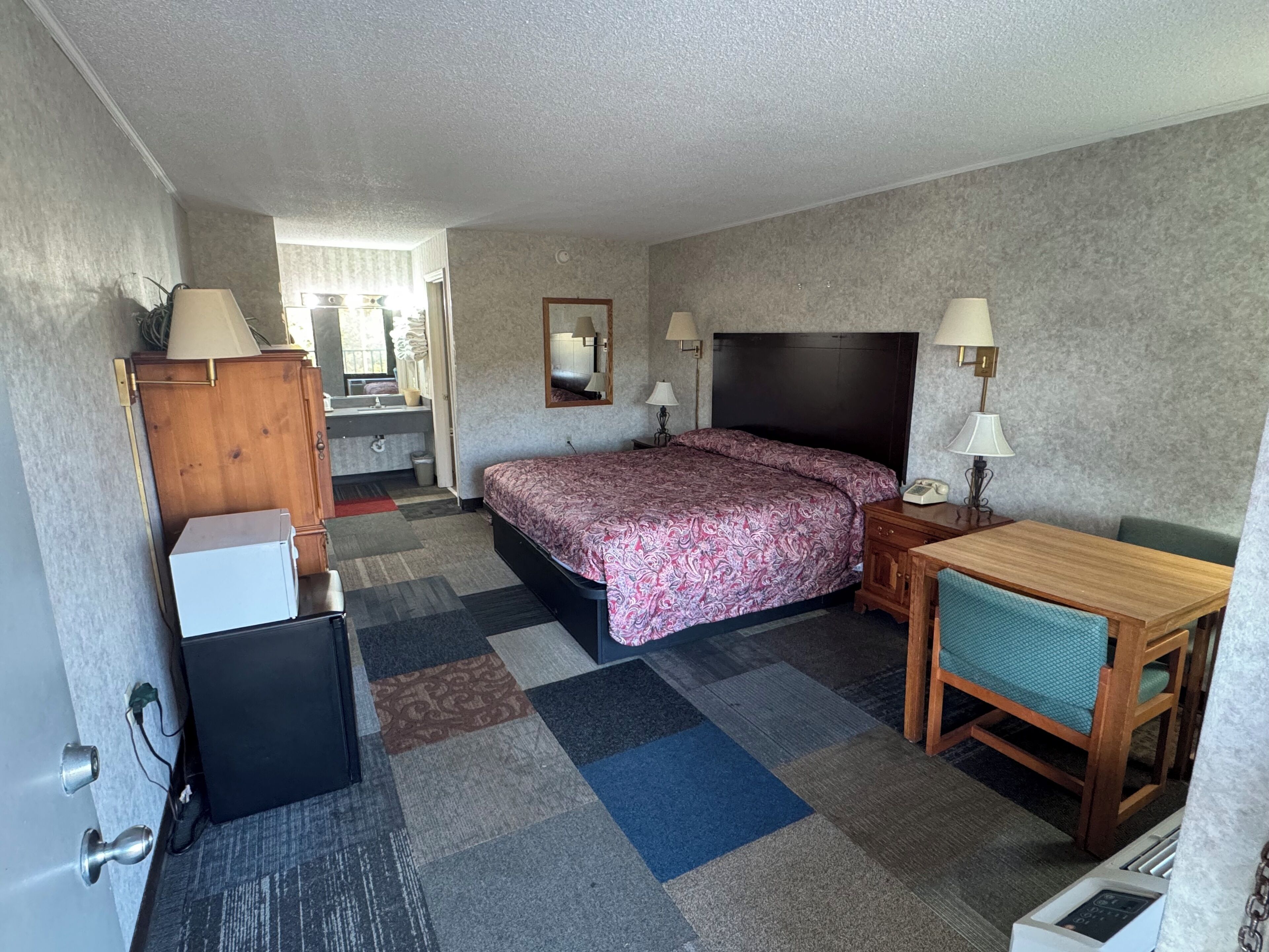 Habitación de hotel con cama, escritorio, silla y una pequeña kitchenette.